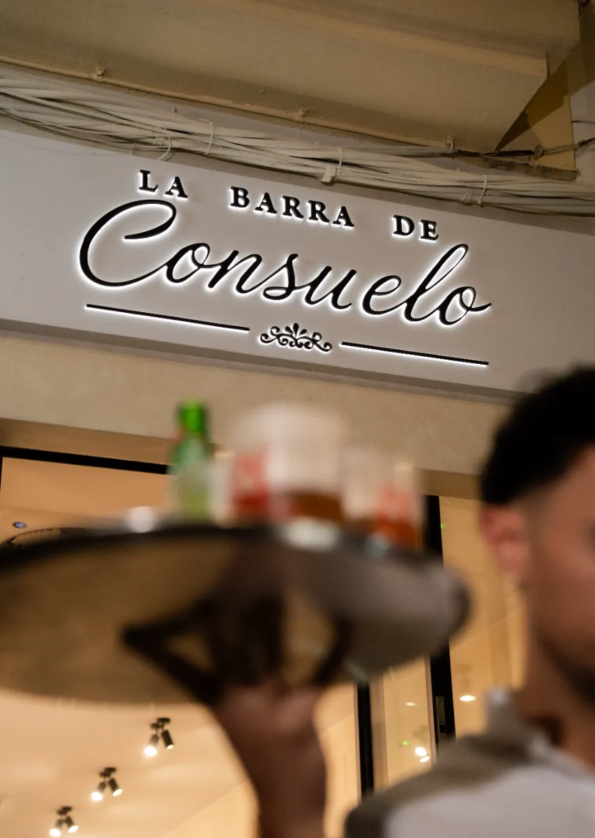 Camarero bajo el rótulo iluminado de La Barra de Consuelo